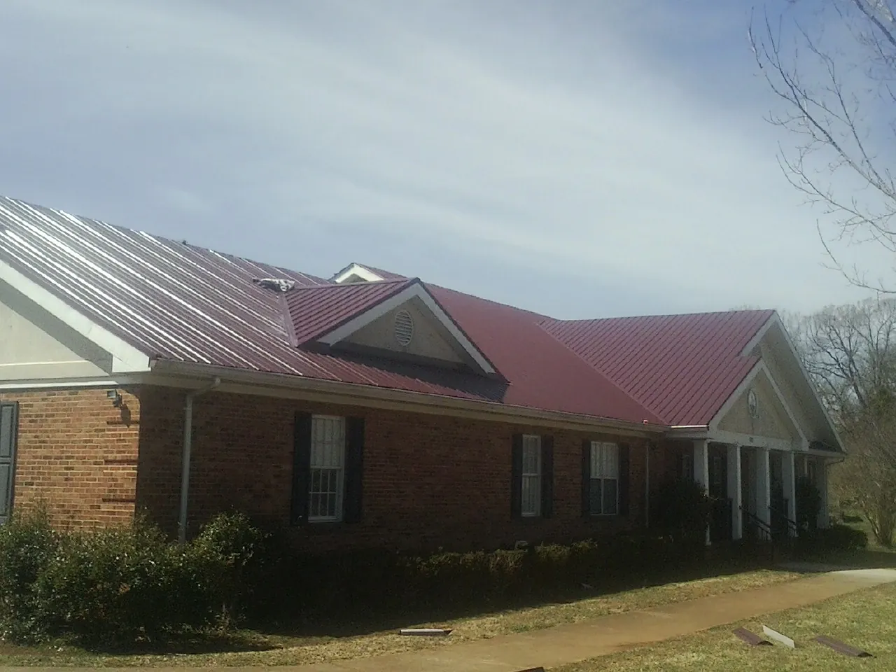 Red metal roof with gabled entries on a long brick building, from a Hail Damage Roof Repair job in Emporia