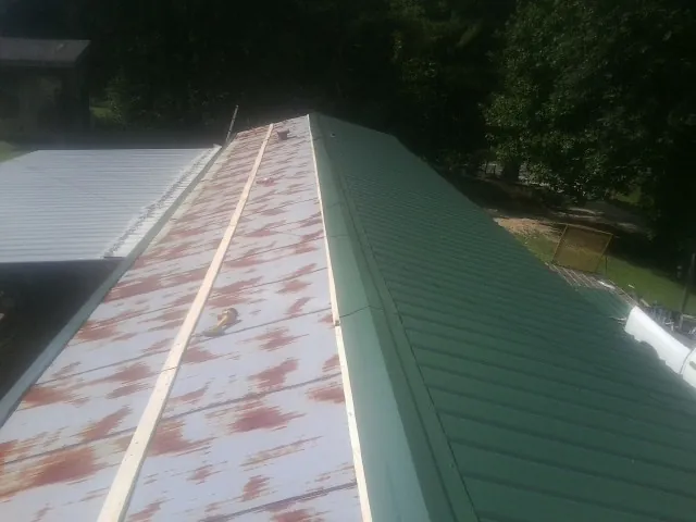 Old rusted panels beside newly installed green metal roofing — Wind Damage Roof Repair by Roofing Brothers in Emporia