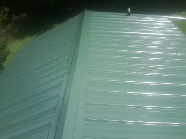 New green metal panels meeting at the ridge of a roof — Flat Roof Repair work by our crew in Emporia
