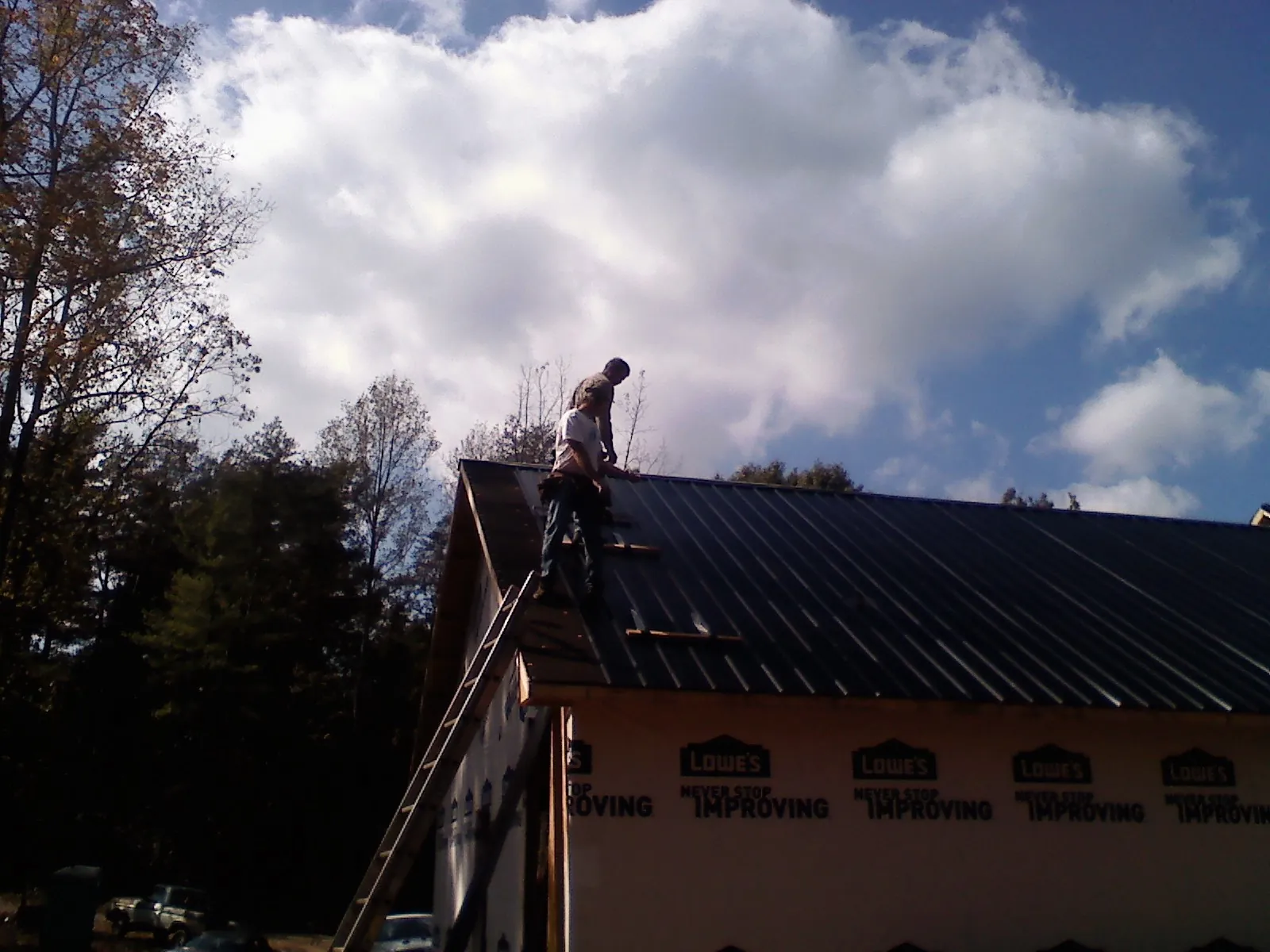 Roofer fastening dark metal panels high against a cloudy sky, from a Roof Inspection job in Emporia