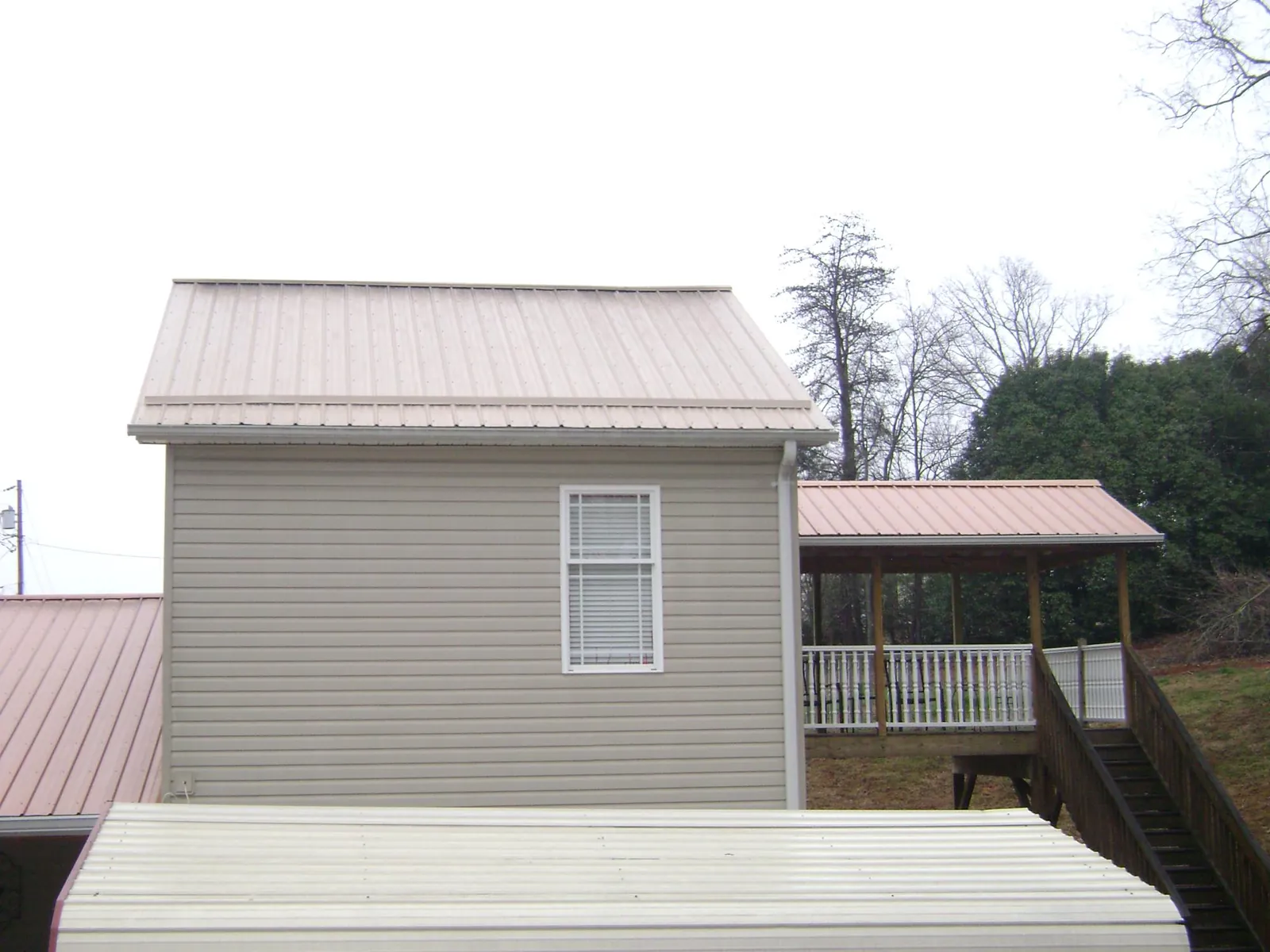Tan metal roofs on a two story addition and attached porch, from a Roof Replacement job in Emporia
